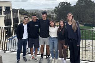 Six students smile together outside on a balcony at the University of San Diego.