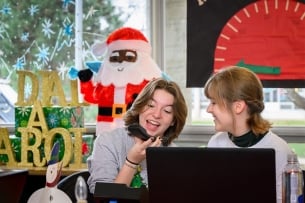 Two students answer the phone singing in a Christmas-decorated room