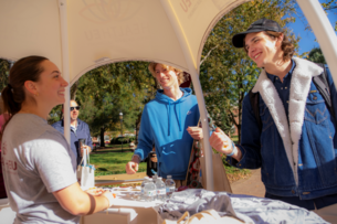 College students engage with a staff member at a booth on Elon University's sunny campus